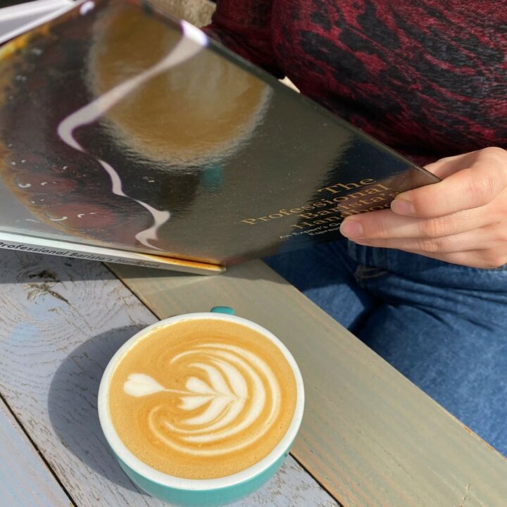 Cliente qui lit en terrasse et son cappuccino avec tulipe en latté art